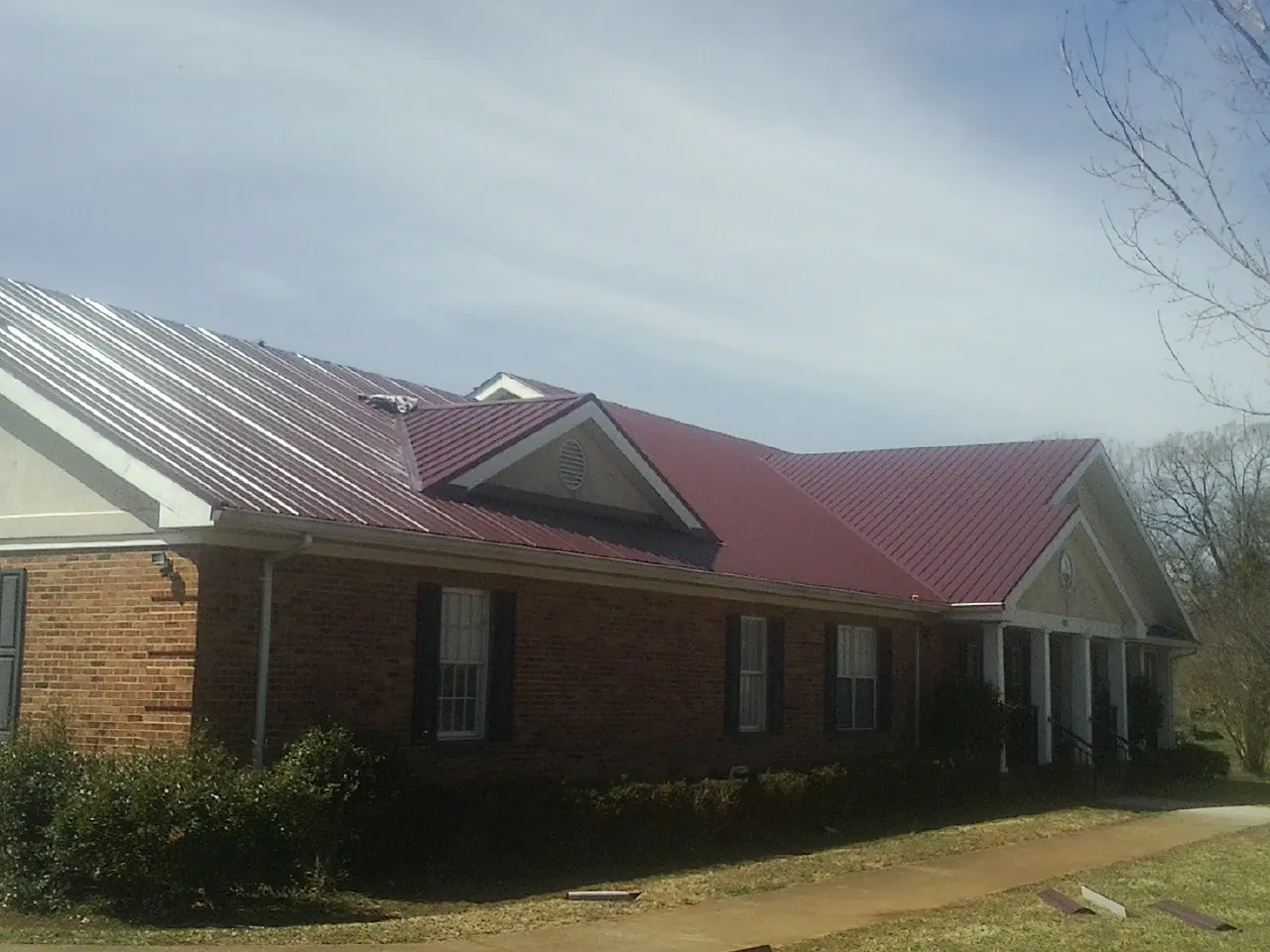 Red metal roof with gabled entries on a long brick building, from a Hail Damage Roof Repair job in Stapleton