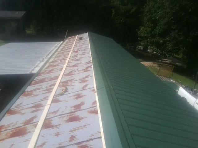 Old rusted panels beside newly installed green metal roofing — Wind Damage Roof Repair by Roofing Brothers in Stapleton