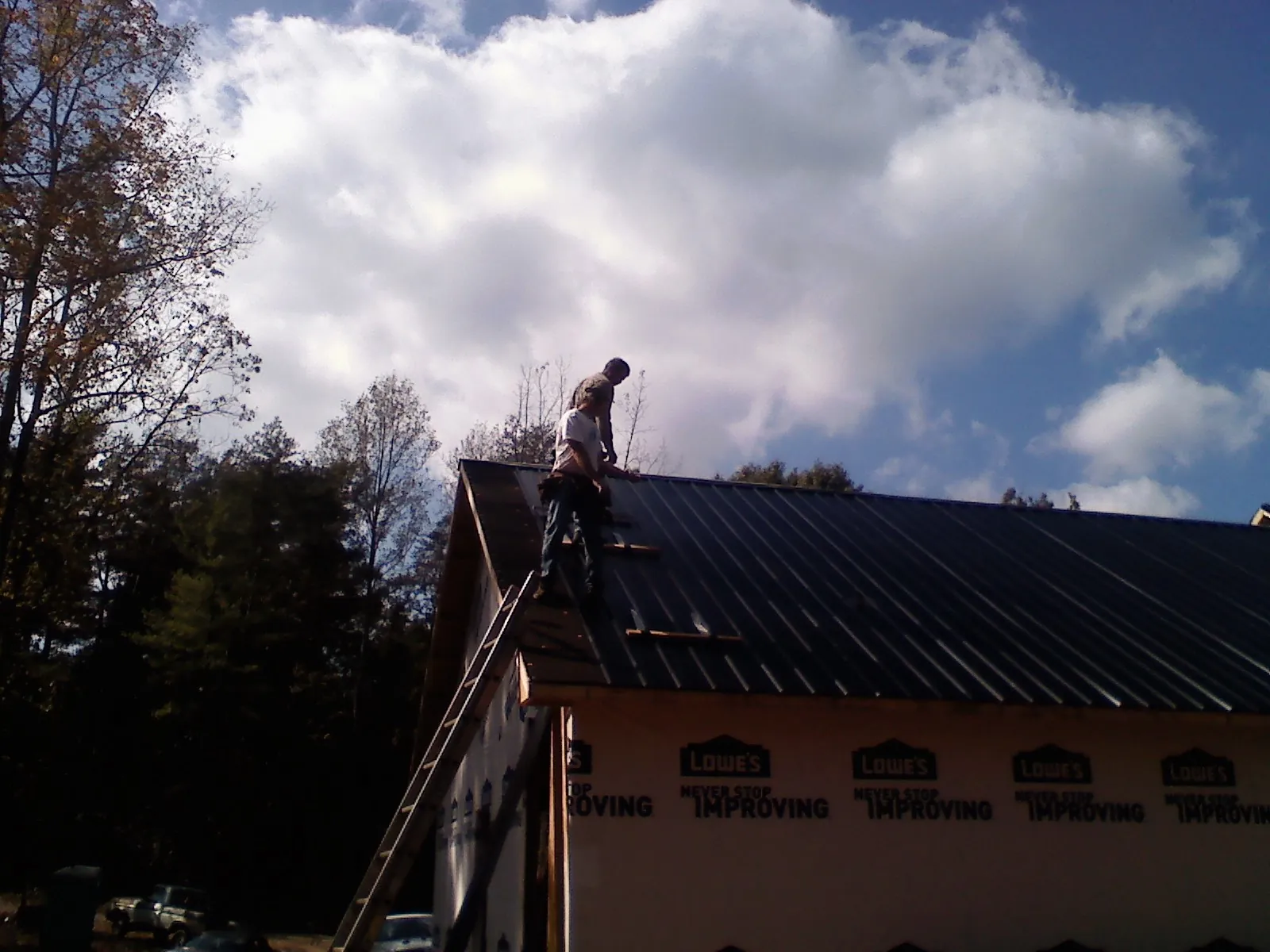 Roofer fastening dark metal panels high against a cloudy sky, from a Roof Inspection job in Stapleton
