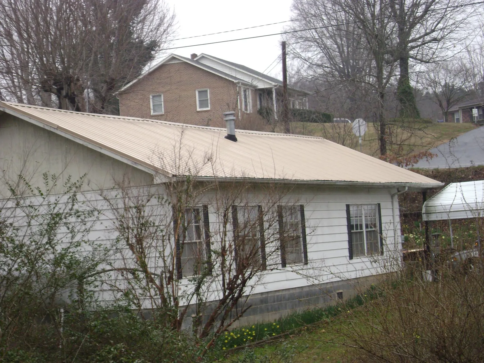 Tan metal roof on a white sided house set into a hillside — Commercial Roofing by Roofing Brothers in Stapleton